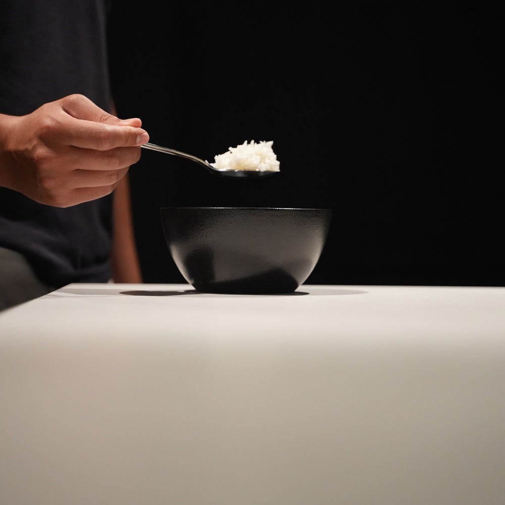 A spoonful of prepared Cut Kitchen rice above a black bowl